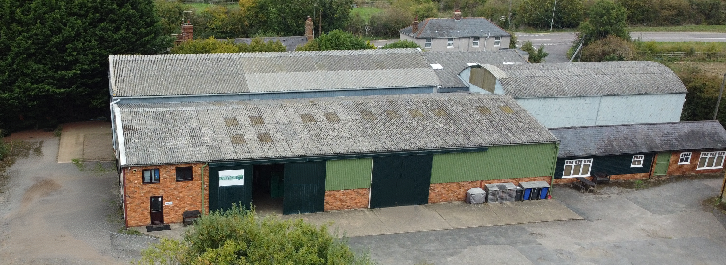 Aerial view of the large Totebox building with a green roof and brick walls, surrounded by trees and other structures.